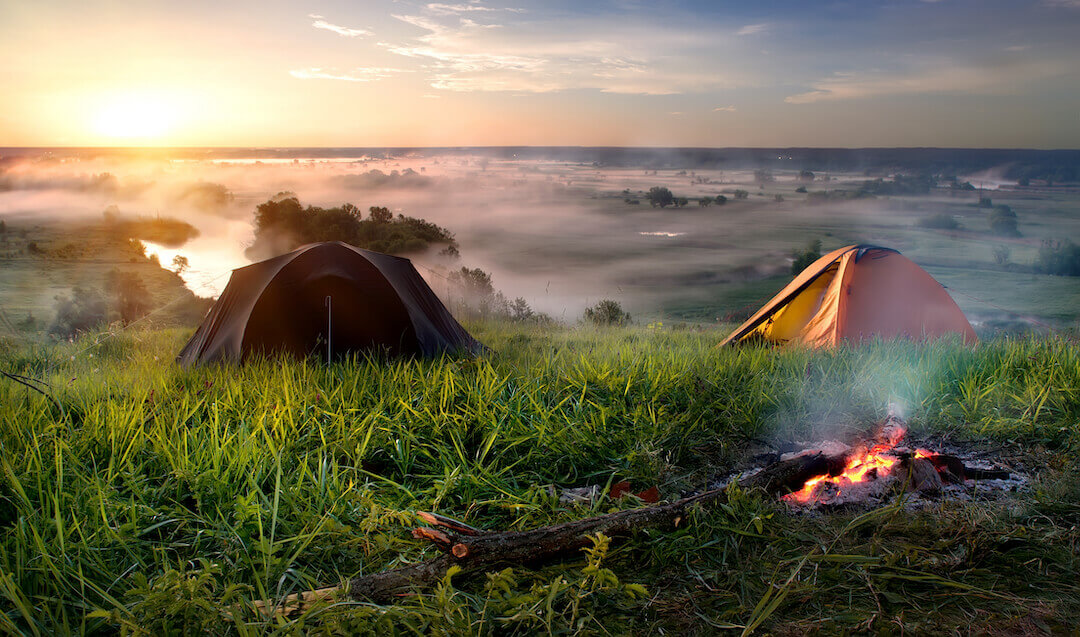 Tentes et feu de camping près d'une rivière à l'aube