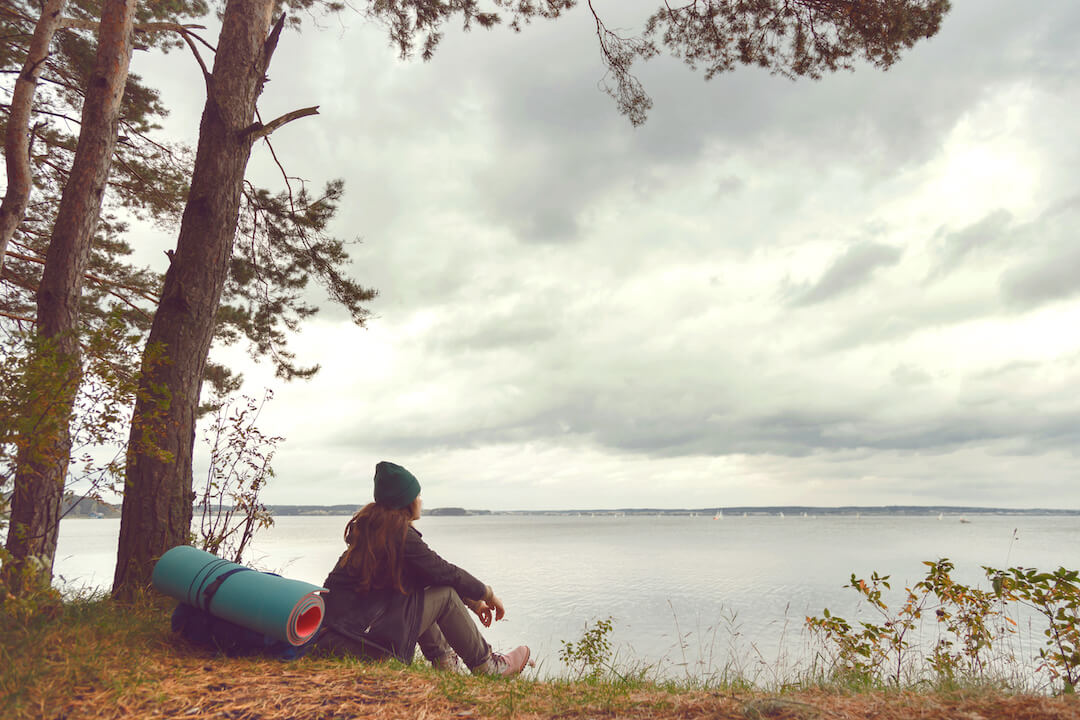 Femme solitaire voyageant assise près d'un lac forestier et regardant loin